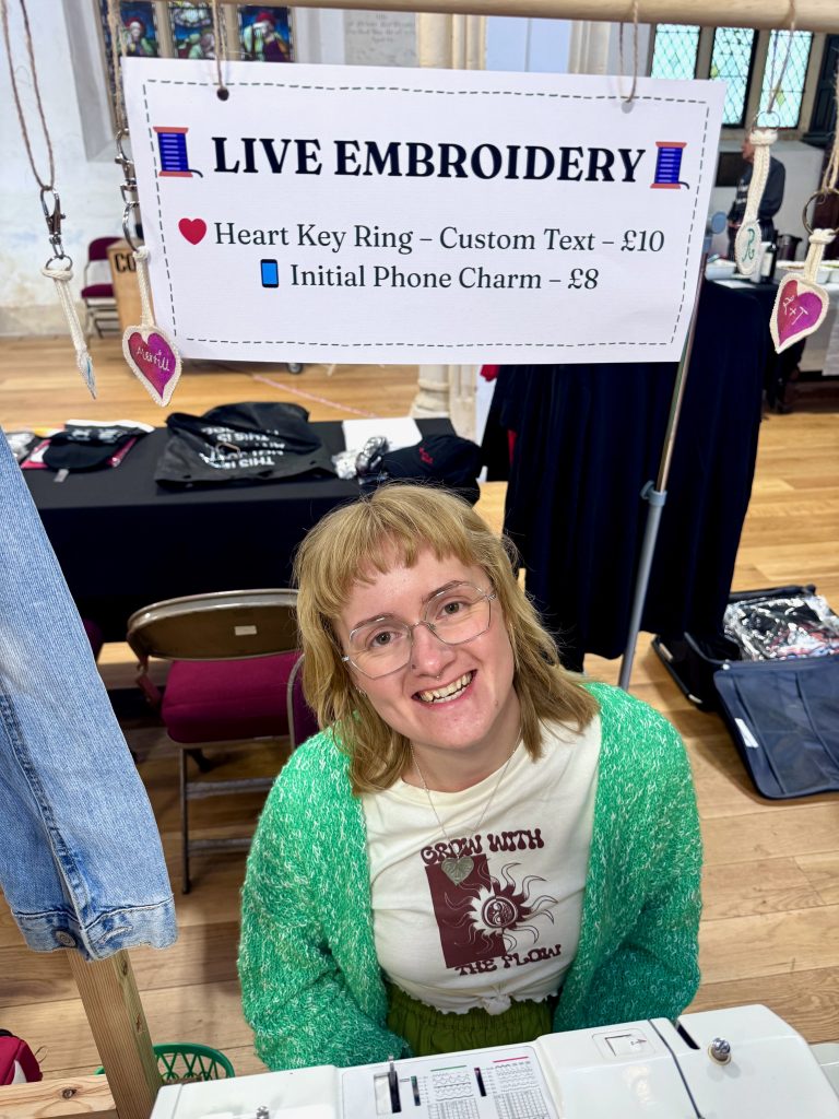 A photo of Lucy Dunster under the Live Embroidery market stall sign