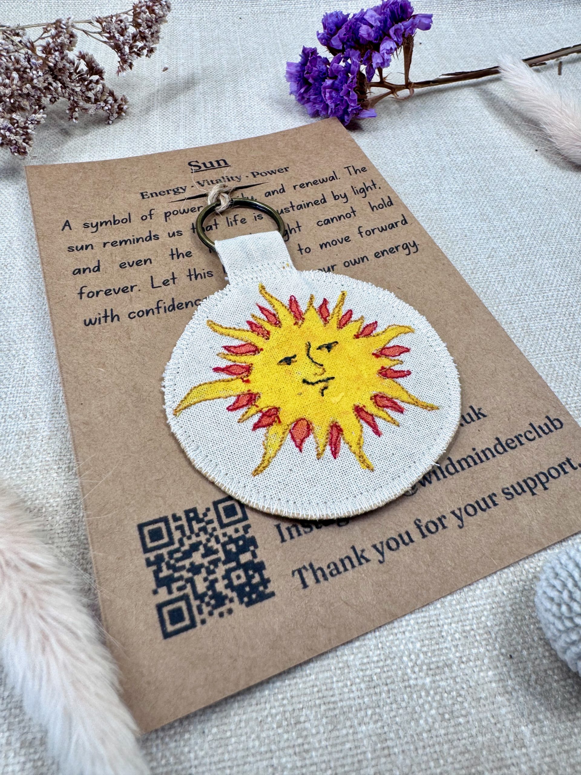 An angled photo of the Wild Minder Sun Talisman Keyring on it's backing oracle card