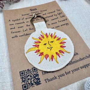 An angled photo of the Wild Minder Sun Talisman Keyring on it's backing oracle card